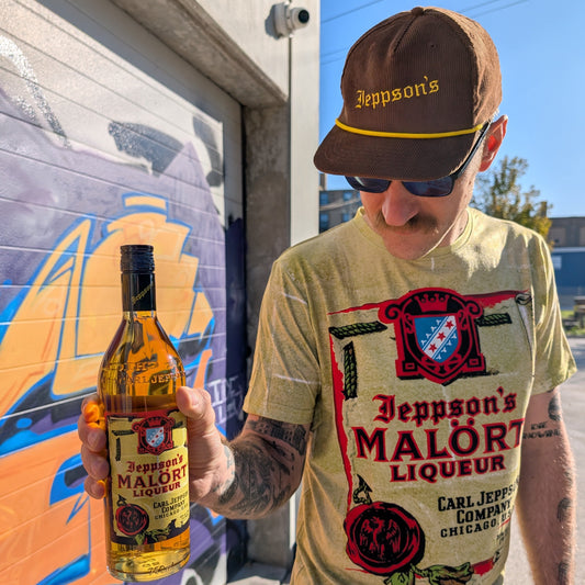 Person holding a bottle of Jeppson's Malört Liqueur in front of a colorful mural.